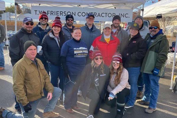 Group of employees gathered outdoors under a T.W. Frierson Contractor, Inc. tent at a winter community event